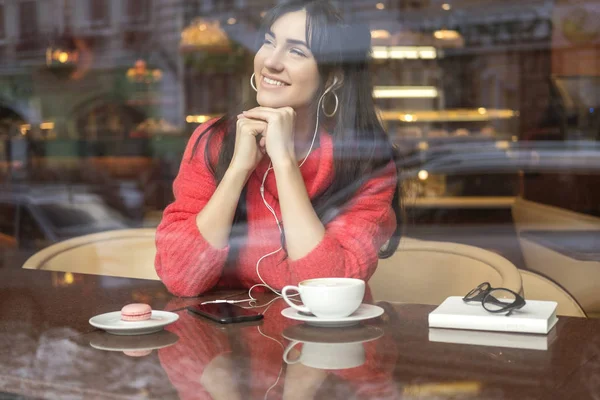 かわいいブルネット プラスサイズの女性 フリーランス の距離に取り組んで カフェに座って コーヒーを飲みながら マカロンを食べてします 赤いセーターを着ている彼女は聞く音楽と彼女の電話でメッセージを入力します — ストック写真