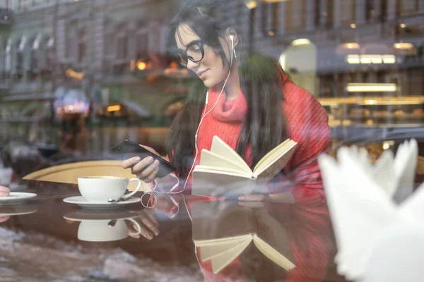 可爱的黑发和大小的女人工作的距离 自由职业者 坐在咖啡馆 喝咖啡和吃 Macaron 她穿着红色毛衣 听音乐 在手机上打字 — 图库照片
