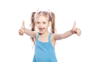 Beyaz izole zemin üzerinde mavi elbiseli Genç yedi yaşında esmer kız. O yüzündeki başparmak yukarıya hareketi elleri, gülümseyen ve mutluluk ve sevinç duygular ile yapmak