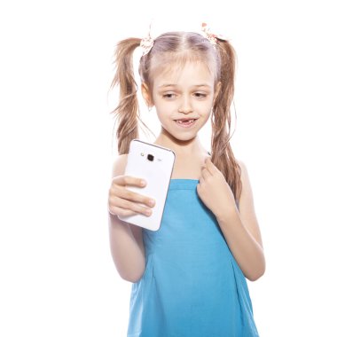 Beyaz izole zemin üzerinde mavi elbiseli Genç yedi yaşında esmer kız. O yüzündeki mobil telefon, eğlenceli ve gülümseme duygularını üzerinde selfie yapar