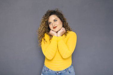 Şirin esmer artı boyutu kadın sarı kazak ve bir nötr gri arka plan üzerinde ayakta kot kıvırcık saçlı. O, yüzünde düşünceli duygu düşünüyordum. Kopya alanı