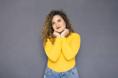 Şirin esmer artı boyutu kadın sarı kazak ve bir nötr gri arka plan üzerinde ayakta kot kıvırcık saçlı. O, yüzünde düşünceli duygu düşünüyordum. Kopya alanı