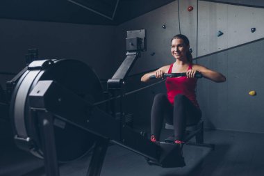 İnce yapılı esmer kadın spor salonunda egzersiz yapıyor, ağırlık kaldırıyor.