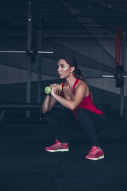 İnce yapılı esmer kadın spor salonunda egzersiz yapıyor, ağırlık kaldırıyor.