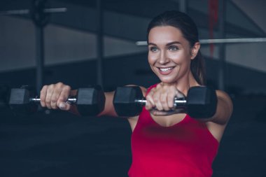 İnce yapılı esmer kadın spor salonunda egzersiz yapıyor, ağırlık kaldırıyor.