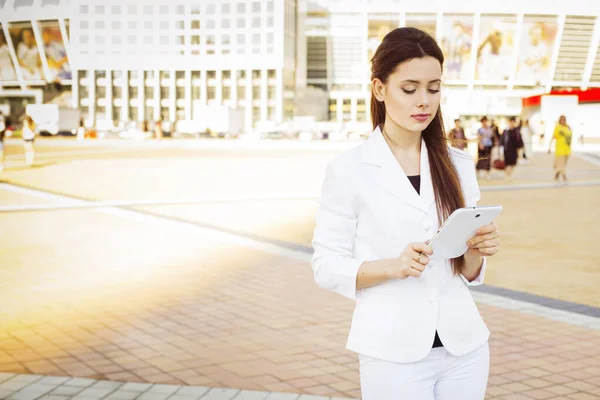 白いスーツを着た美しいブルネットのビジネス女性が屋外でタブレットで働いています コピースペース — ストック写真
