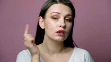 Tarafsız giysiler içinde pembe arka planda duran seksi esmer beyaz kadın. Hangi ses tonunu kullanacağına o karar veriyor. Kozmetik kavramı