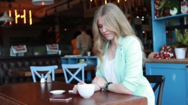 Yazın bir kafe terasında oturan, kahve içen ve birini bekleyen şık bir kadın. Seksi, sevimli, gülümseyen sarışın kamera önünde poz veriyor ve flört ediyor.