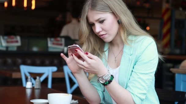 Vrouw in de zomer slim casual outfint zitten op een cafe terras, het drinken van koffie en werken in sociale media op haar telefoon. Sexy schattig glimlachen blond poseren en flirten op camera — Stockvideo