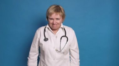 Beyaz önlüklü, mavi arka planda, Kafkasyalı, yaşlı bir doktor. Steteskop takıyor ve sinirleniyor. Ağlıyor.