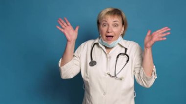 Beyaz önlüklü, mavi arka planda, Kafkasyalı, yaşlı bir doktor. Steteskop takıyor ve hareketler yapıyor.