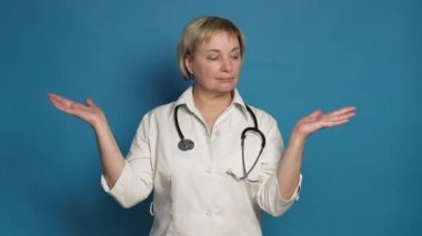 Beyaz önlüklü, mavi arka planda, Kafkasyalı, yaşlı bir doktor. Steteskop takıyor ve seçici hareketler yapıyor.