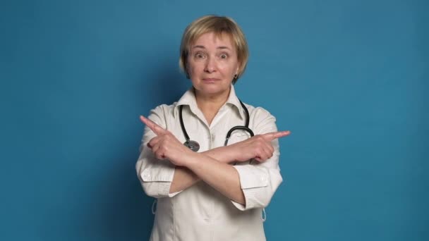Eldery caucasiano dama de médico em casaco branco no fundo azul. Ela usa estetoscópio e aponta os dedos. — Vídeo de Stock