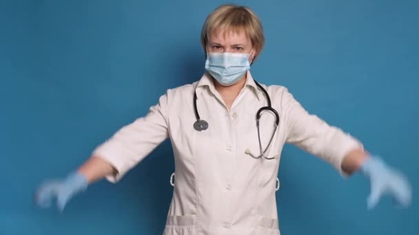 Oudere blanke dokter dame in witte jas op blauwe achtergrond. Ze draagt stethoscoop en maakt duimen naar beneden / afkeer van gebaren — Stockvideo