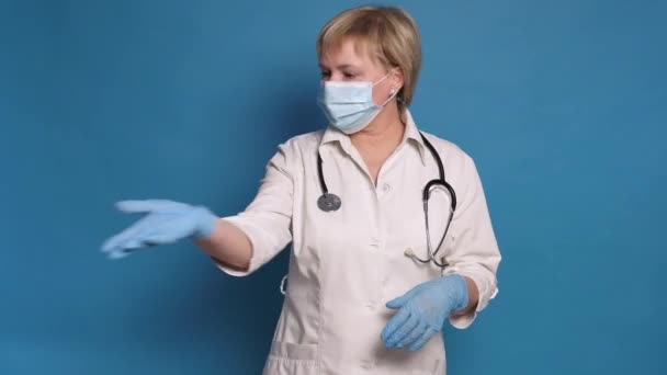 Oudere blanke dokter dame in witte jas op blauwe achtergrond. Ze draagt stethoscoop en praat op camera. — Stockvideo