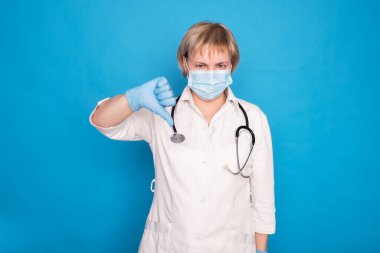 Beyaz önlüklü, yaşlı, beyaz saçlı, mavi arka planda steteskoplu bir doktor. Duygusal portreler, baş parmaklar..