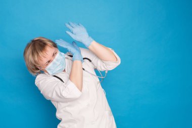 Beyaz önlüklü, yaşlı, beyaz saçlı, mavi arka planda steteskoplu bir doktor. Duygusal portreler: korkmuş, elleriyle kaplamış..