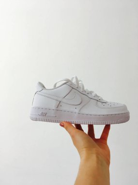 Beyaz Nike Hava Kuvvetleri spor ayakkabıları beyaz bir duvara karşı bir kadın elinde