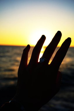 Gün batımında deniz kıyısında bir kızın eli