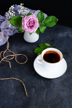 kahve fincanı ve pembe gül masanın üstünde vazoda.