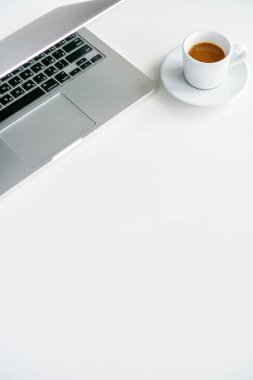 kahve fincanı ve gri laptop beyaz arka planda masanın üstünde.