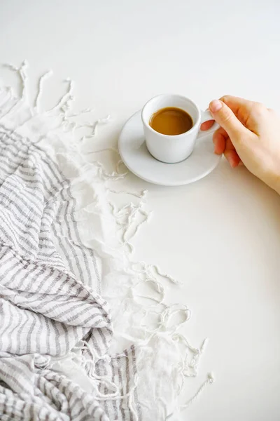 Kadın elleri kahve fincanı ve çay tabağını beyaz bir masanın üzerinde tutuyor.