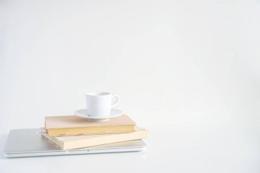 Kitaplar gri bir dizüstü bilgisayarda, üzerinde bir kupa kahve ve bir vazo çiçeğin yanında.