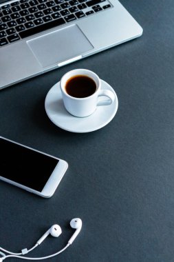 cep telefonu, kahve fincanı, kulaklık ve dizüstü bilgisayar siyah arka planda.