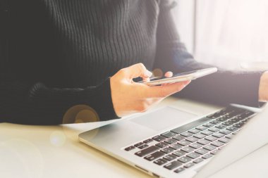 Bir kız elinde bir telefon, yanında bir laptop duruyor ve gözlük yalan söylüyor.