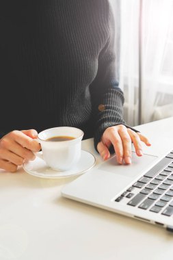 Kız dizüstü bilgisayarda klavyeyle yazı yazıyor, sırada bir kupa kahve var.