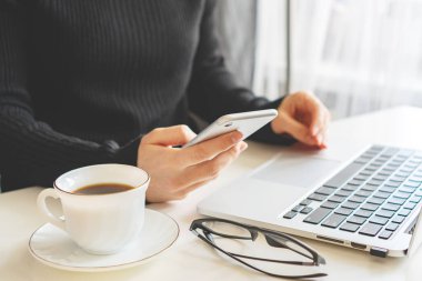 Bir kız elinde bir telefon, yanında bir laptop duruyor ve gözlük yalan söylüyor.