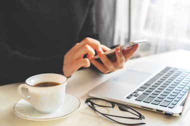 Bir kız elinde bir telefon, yanında bir laptop duruyor ve gözlük yalan söylüyor.
