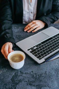 Kız dizüstü bilgisayarda klavyeyle yazı yazıyor, sırada bir kupa kahve var.