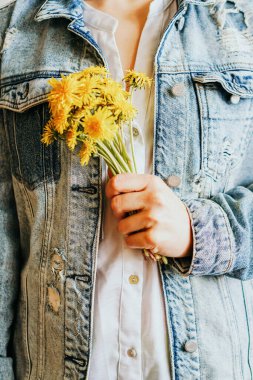 Kırmızı ceketli kız elinde sarı karahindiba tutuyor.