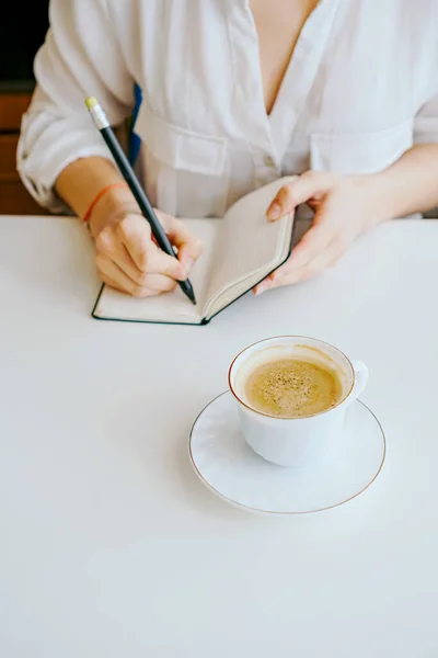 girl makes notes in a notebook, next is a coffee mug