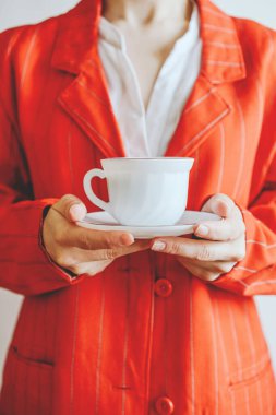 Kırmızı ceketli kız elinde bir kupa kahve tutuyor.