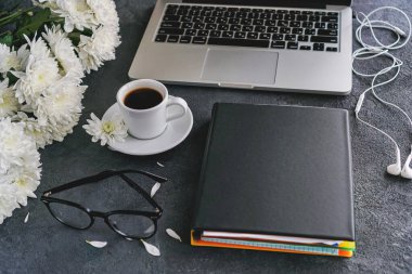 Masanın üstünde siyah bir arka planda dizüstü bilgisayar ve kahve fincanı var. Yanında notlar ve gözlükler için bir not defteri var.