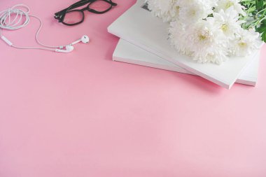 Pembe arka planda dergiler, kulaklıklar ve kasımpatı çiçekleri var.