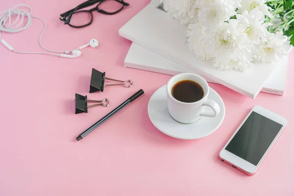 coffee mug, magazines, flowers and glasses lie on a table on a pink background