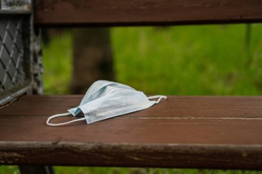 Virüsten korunmak için parktaki bankta duran koruyucu bir maske.