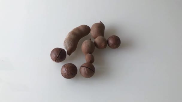 Орехи макадамии и спелые плоды тамаринда, разбросанные по столу. Медленное движение . — стоковое видео