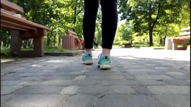 Şehirde yürüyen kadın ayaklarının ayrıntıları. Dişi bacaklar kirli bir taş patika boyunca yeşil spor ayakkabılarla yürür..
