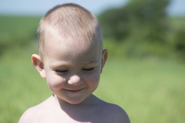 Uzun otların arasında yeşil bir çayırda oynayan sevimli sarışın çocuk.