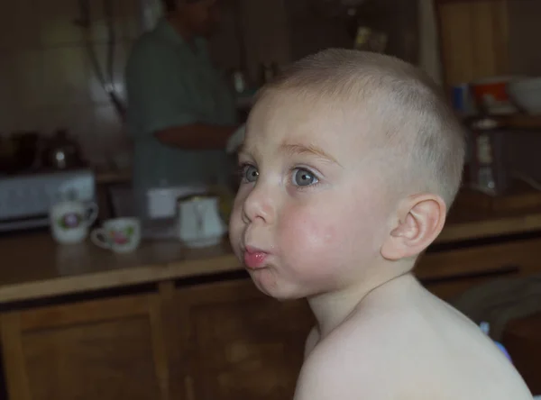 Cute blond child eats in the kitchen, cucumber juice flows on the cheeks — Stock Photo, Image