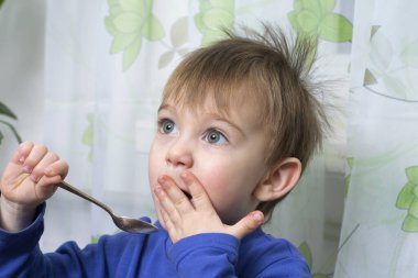 İki yaşındaki güzel bebeğin kaşıkla yemek yemesine yakın durun.