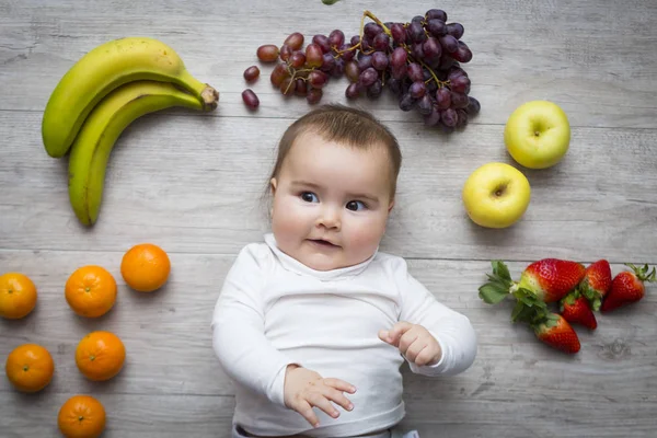 Маленький ребенок на полу с разноцветными фруктами — стоковое фото