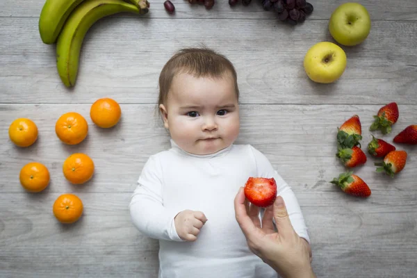 Маленький ребенок на полу с разноцветными фруктами — стоковое фото