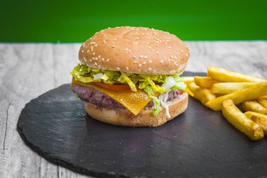 Ev hamburguer kaşar peyniri ile yapılmış, domates, marul, servis kişiler üzerine bir yazı tahtası üzerinde gri ahşap masa ile. Hipster burger