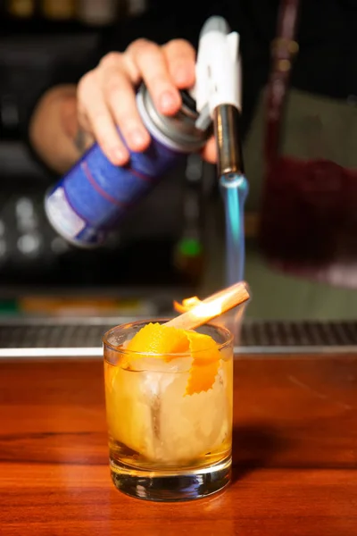 Barman spálí skořicovou tyčinku s plynovým hořákem v baru. — Stock fotografie