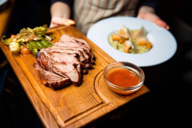 Freshly prepared meat steak sliced into pieces on a wooden board.